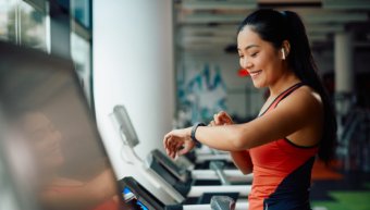 Happy Asia athletic woman uses fitness tracker while running on treadmill in gym.