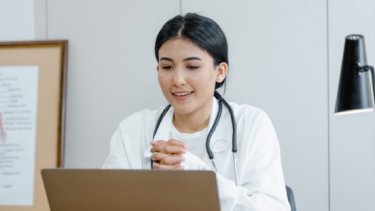 a woman in a white coat looking at a laptop