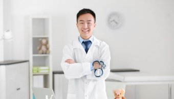 A doctor in white coat standing by a desk with a laptop