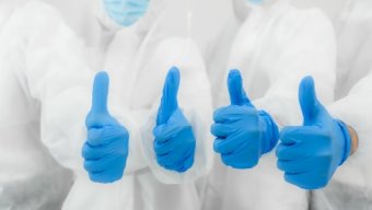 Four people in white suits with blue gloves giving thumbs up