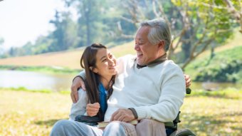 An older man in a wheelchair with a young woman, showing care and support in their companionship