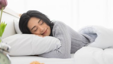 A woman peacefully sleeping in bed, surrounded by pillows and flowers