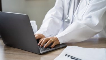 A doctor sitting at a desk with a laptop open in front of them